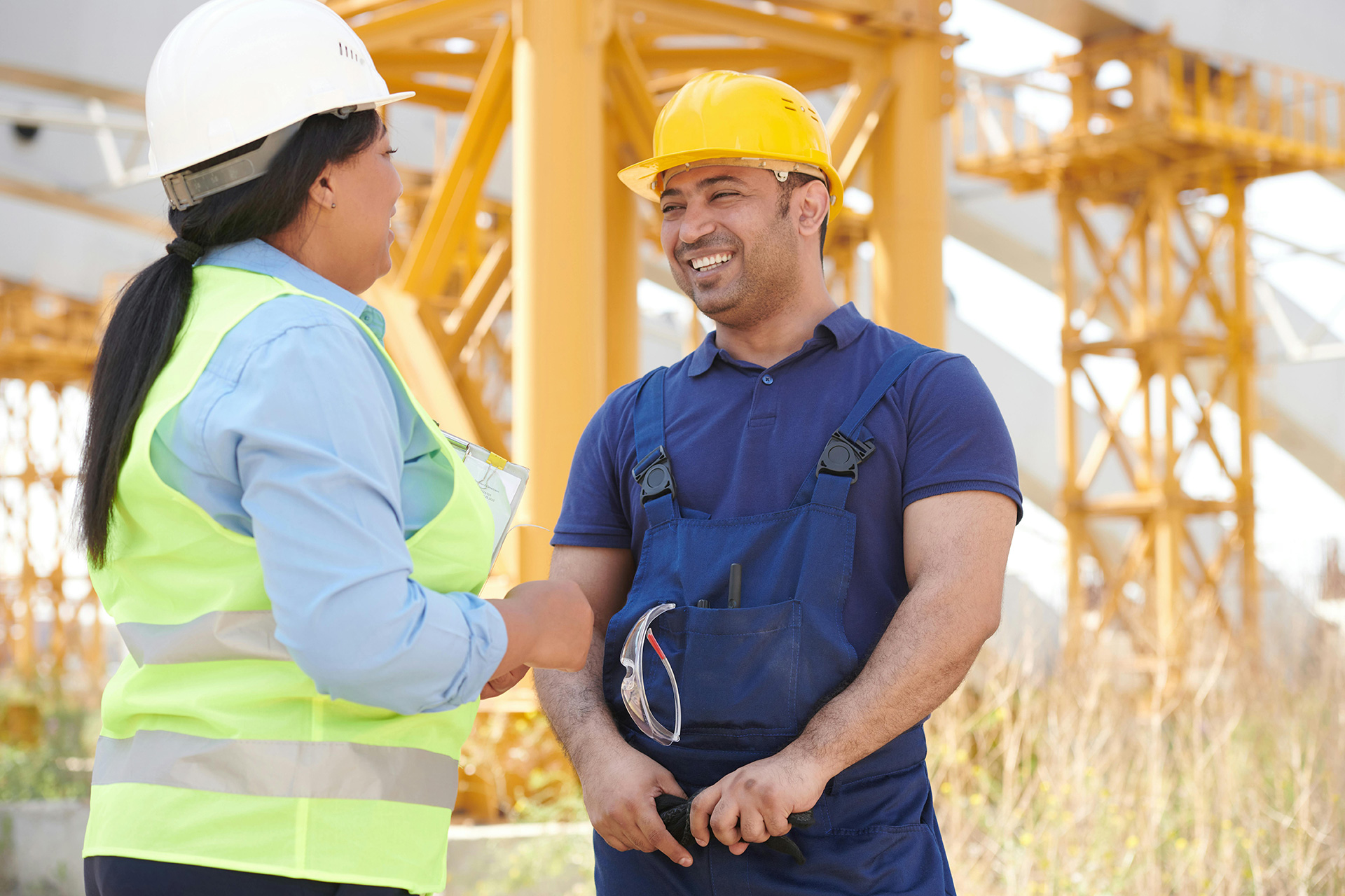 Two site workers smiling at each other, with a crane in the background