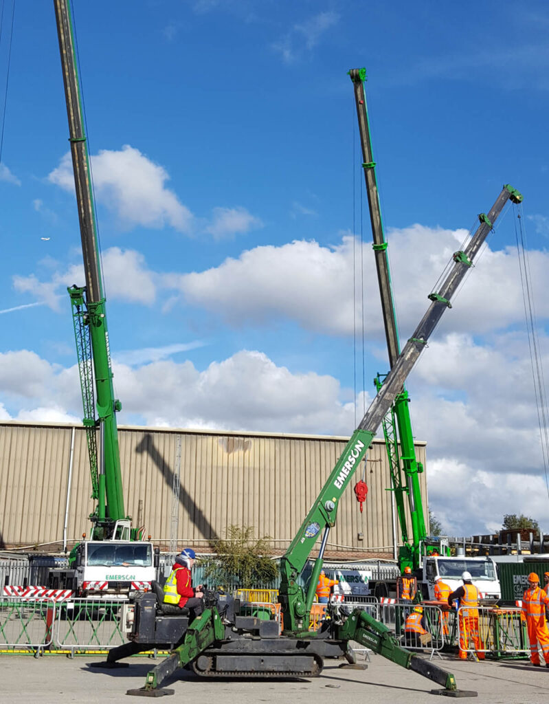 Three green spider cranes on site with Emerson Cranes branding and several workers in hi viz around them